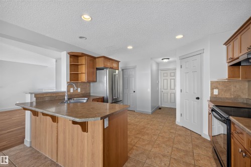 Kitchen featuring a peninsula island, stainless steel refrigerator, black range, tile flooring, and wood-finish cabinetry - 6116 8 Avenue Sw, Edmonton, AB 