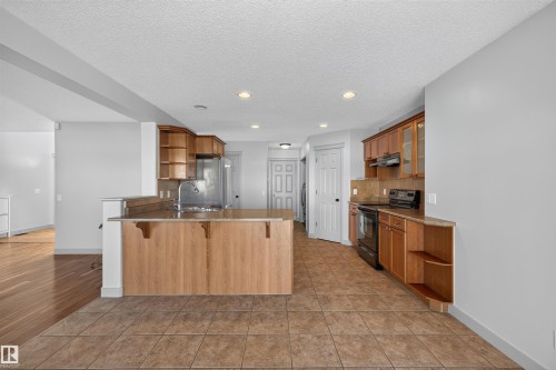 Kitchen featuring wood cabinetry, stainless steel sink, black range, and tile flooring - 6116 8 Avenue Sw, Edmonton, AB 