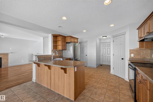 Kitchen featuring wood cabinetry, stainless steel appliances, tile flooring, and a kitchen island with sink - 6116 8 Avenue Sw, Edmonton, AB 