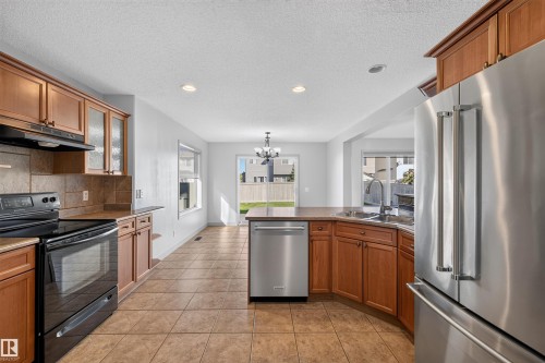 Kitchen featuring wood-finish cabinetry, tile backsplash, built-in stainless steel appliances, and tile flooring - 6116 8 Avenue Sw, Edmonton, AB 