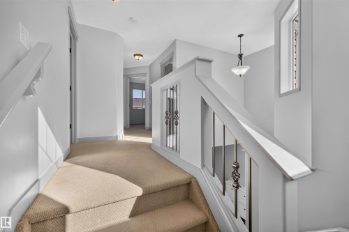 Carpeted staircase with white painted railing, decorative metal balusters, and overhead lighting - 6116 8 Avenue Sw, Edmonton, AB 