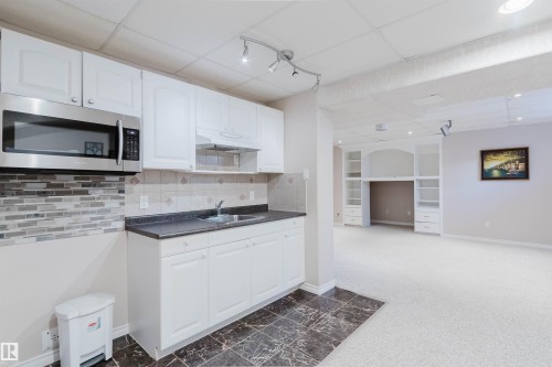 Kitchenette featuring white cabinetry, stainless steel microwave, stone-look backsplash, and dark countertops - 11526 9 Avenue Nw, Edmonton, AB 
