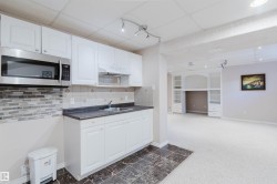 Kitchenette featuring white cabinetry, stainless steel microwave, stone-look backsplash, and dark countertops - 