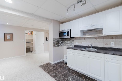 White cabinetry with dark countertops, stainless steel microwave, and tile backsplash - 11526 9 Avenue Nw, Edmonton, AB 