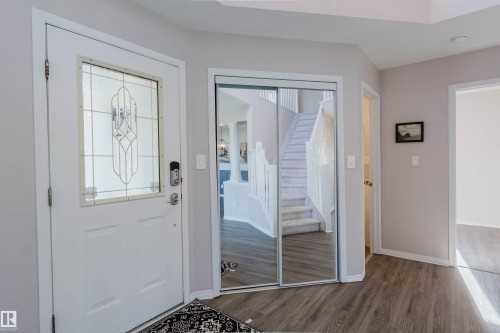Entryway featuring wood-finish flooring, a white front door with decorative glass inlay, and mirrored closet doors - 11526 9 Avenue Nw, Edmonton, AB 