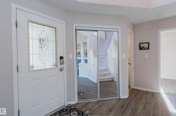 Entryway featuring wood-finish flooring, a white front door with decorative glass inlay, and mirrored closet doors - 