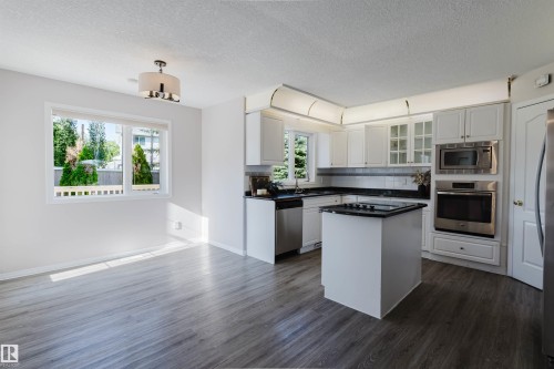 Kitchen with white cabinetry, stainless steel appliances, a center island with a cooktop, and dark countertops - 11526 9 Avenue Nw, Edmonton, AB 