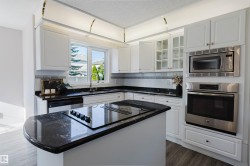 White cabinetry, dark stone countertops, stainless steel appliances, kitchen island, and wood-finish flooring - 