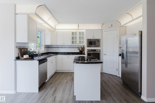 White cabinetry, dark stone countertops, stainless steel appliances, wood-finish flooring, and recessed lighting - 11526 9 Avenue Nw, Edmonton, AB 