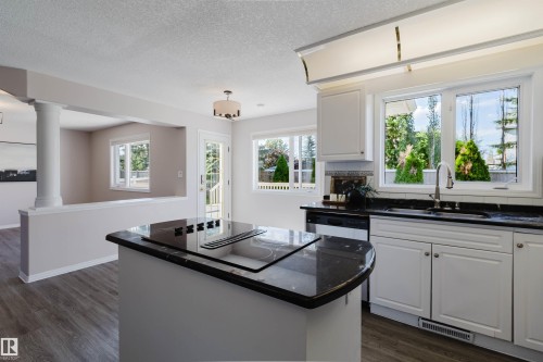 Kitchen featuring a center island with integrated cooktop, white cabinetry, dark stone countertops, and wood-finish flooring - 11526 9 Avenue Nw, Edmonton, AB 