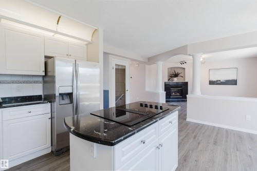 Kitchen with white cabinetry, black stone-finish countertops, stainless steel side-by-side refrigerator, and an island cooktop - 11526 9 Avenue Nw, Edmonton, AB 