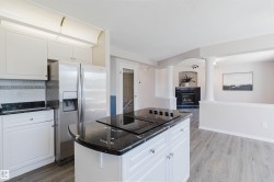 Kitchen with white cabinetry, black stone-finish countertops, stainless steel side-by-side refrigerator, and an island cooktop - 