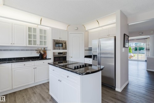 Kitchen featuring white cabinetry, dark countertops, wood-finish flooring, a central island with a cooktop, and stainless steel appliances - 11526 9 Avenue Nw, Edmonton, AB 