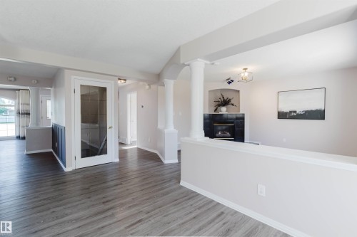 Wood-finish flooring throughout, white interior columns, built-in fireplace with black surround, white half-wall partition, and a glass-paneled interior door - 11526 9 Avenue Nw, Edmonton, AB 