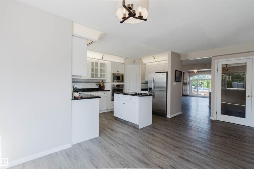Kitchen featuring white cabinetry, dark countertops, a central island, stainless steel appliances, and wood-finish flooring - 11526 9 Avenue Nw, Edmonton, AB 