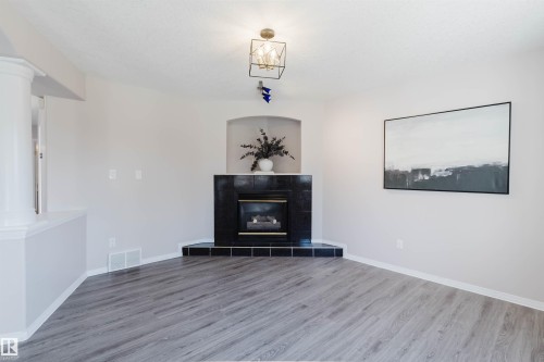 Wood-finish flooring, corner fireplace with a black tile surround, recessed alcove, and a decorative ceiling light fixture - 11526 9 Avenue Nw, Edmonton, AB 
