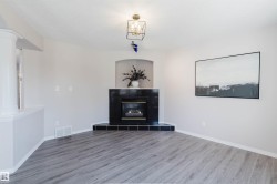 Wood-finish flooring, corner fireplace with a black tile surround, recessed alcove, and a decorative ceiling light fixture - 