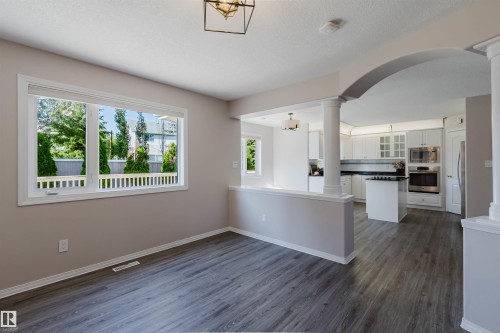 Spacious interior featuring wood-finish flooring, a large window, and an arched entry with decorative columns - 11526 9 Avenue Nw, Edmonton, AB 