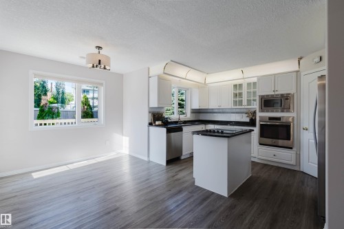 Open concept kitchen with white cabinetry, stainless steel appliances, black countertops, and a central island - 11526 9 Avenue Nw, Edmonton, AB 