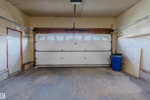 Single-car garage with a paneled overhead door, upper transom windows, concrete flooring, and a side entry door - 11526 9 Avenue Nw, Edmonton, AB 
