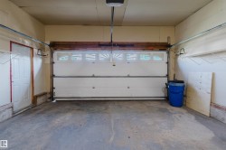 Single-car garage with a paneled overhead door, upper transom windows, concrete flooring, and a side entry door - 