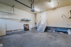 Spacious garage featuring a concrete floor, overhead lighting, garage door opener, and interior access door with stairs - 