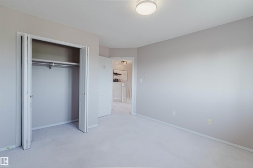 Neutral-toned room featuring a flush-mount ceiling light, light-colored carpeting, and a bi-fold door closet with a hanging rod - 11526 9 Avenue Nw, Edmonton, AB 