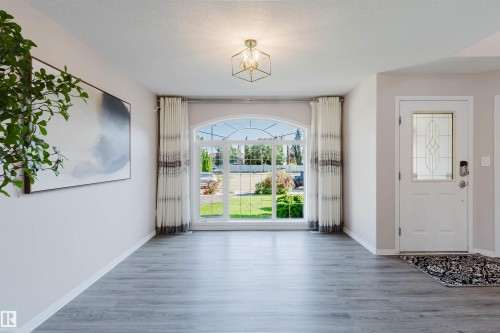 Arched window with exterior landscaping, wood-finish flooring, contemporary geometric light fixture, and a front entry door with decorative glass inlay - 11526 9 Avenue Nw, Edmonton, AB 