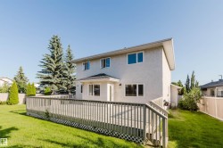 Expansive wooden deck with railing, stucco exterior, multiple windows, and a manicured lawn - 