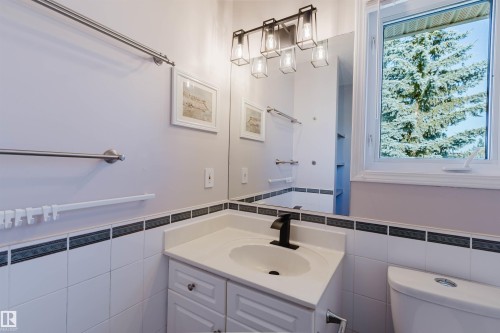 Bright bathroom featuring a white vanity with an undermount sink, matte black faucet, and white subway tile with contrasting dark tile trim - 11526 9 Avenue Nw, Edmonton, AB 