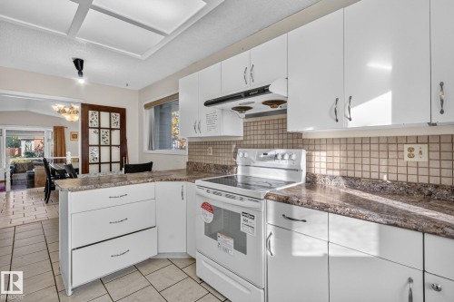 White cabinetry, patterned backsplash, solid surface countertops, white electric range, and light-toned tile flooring - 11 Howson Crescent Nw, Edmonton, AB 