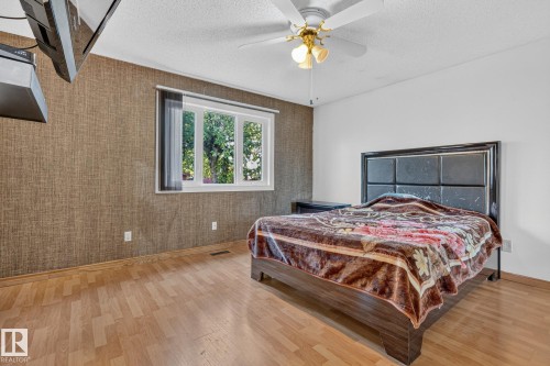 Wood-finish flooring, textured accent wall, multi-pane window, ceiling fan with integrated lighting, and white painted walls - 11 Howson Crescent Nw, Edmonton, AB 