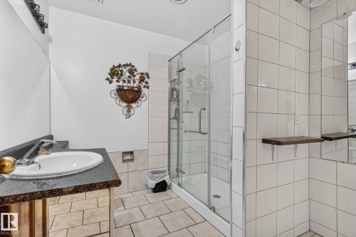 Vanity with a granite-look countertop and integral sink, glass-enclosed shower, white tiled walls, and tiled flooring - 11 Howson Crescent Nw, Edmonton, AB 