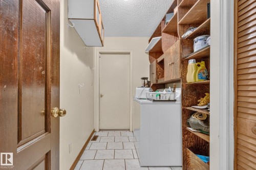 Integrated laundry area featuring wood-finish built-in shelving, a cabinet, and tiled flooring - 11 Howson Crescent Nw, Edmonton, AB 