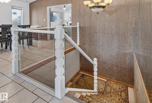 Glass panel railing with white balusters, textured wall covering, tiled flooring, and a chandelier - 11 Howson Crescent Nw, Edmonton, AB 