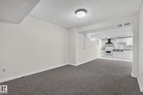 Open-concept living area featuring gray carpeting and a kitchen with white cabinetry, stainless steel appliances, and a dark countertop - 11 Howson Crescent Nw, Edmonton, AB 