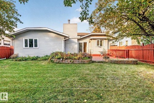 Expansive green space with a red-stained wood fence, an elevated wood deck, and built-in landscape beds - 11 Howson Crescent Nw, Edmonton, AB 