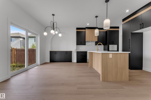 Wood-finish flooring throughout, modern kitchen island with white countertop, black and wood-finish cabinetry, contemporary pendant lighting, and sliding glass patio doors - 58 Silverstone Drive, Stony Plain, AB 