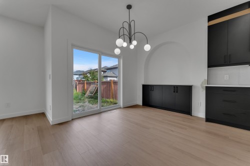 Wood-finish flooring, sliding glass patio door, arched wall niche, built-in black cabinetry, and a modern chandelier - 58 Silverstone Drive, Stony Plain, AB 