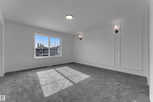 Expansive room with neutral carpeting, prominent window, decorative wall molding, two wall sconces, and a flush-mount ceiling fixture - 58 Silverstone Drive, Stony Plain, AB 