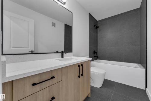 Light wood-finish vanity with black hardware, white countertop, integrated sink with black faucet, and a large framed mirror - 58 Silverstone Drive, Stony Plain, AB 