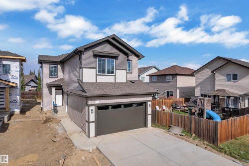 Two-story exterior with horizontal siding, attached garage, concrete driveway, and a wood privacy fence - 58 Silverstone Drive, Stony Plain, AB 