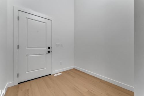 Light wood-finish flooring with white baseboards and a paneled white door featuring black hardware - 58 Silverstone Drive, Stony Plain, AB 
