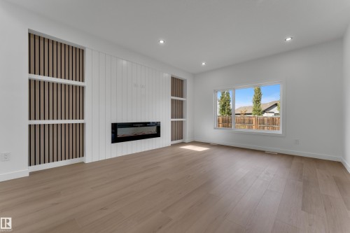 Recessed ceiling lighting, wood-finish flooring, electric fireplace, built-in shelving with vertical slat detailing, and a large window - 58 Silverstone Drive, Stony Plain, AB 