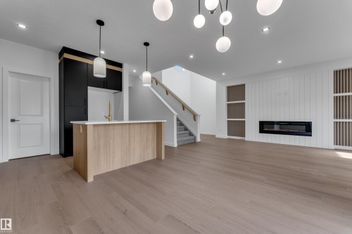 Open-concept living space featuring wood-finish flooring, a contemporary linear electric fireplace, a kitchen island with a light-toned countertop, and integrated ceiling lighting - 58 Silverstone Drive, Stony Plain, AB 