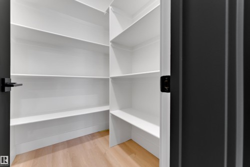 Walk-in pantry with light wood-finish flooring, white built-in shelving, and dark hardware - 261 Linden Loop, Leduc, AB 