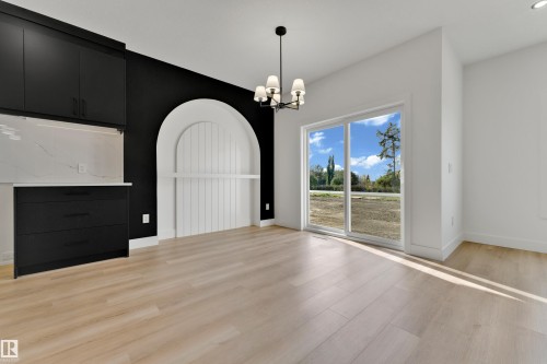 Wood-finish flooring, built-in black cabinetry with white countertop, white arched wall feature, modern chandelier, and sliding glass door - 261 Linden Loop, Leduc, AB 