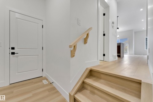 Hardwood flooring throughout, modern white doors with black hardware, natural wood handrail, recessed lighting, and white baseboards - 261 Linden Loop, Leduc, AB 