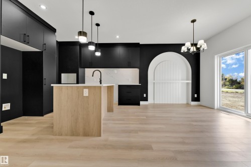 Modern kitchen featuring black cabinetry, light wood-finish flooring, a kitchen island with pendant lighting, white countertops, and a built-in arched feature - 261 Linden Loop, Leduc, AB 