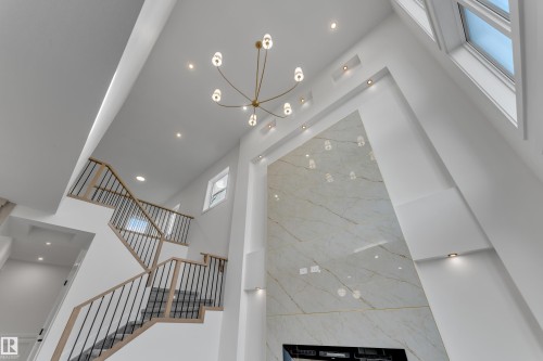 Vaulted ceilings with recessed lighting, a modern chandelier, and a two-story accent wall with a stone-look finish - 247 Linden Loop, Leduc, AB 
